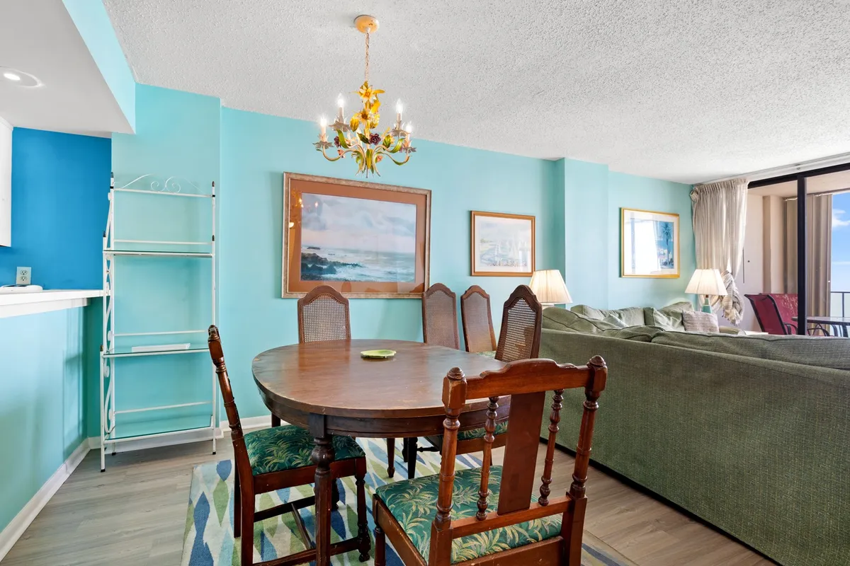 A welcoming open-plan area showcases a dining table under a chandelier, with a seating area and vibrant wall art nearby. The layout encourages gathering for meals, games, or conversation, and the light-filled room feels perfect for family interaction.