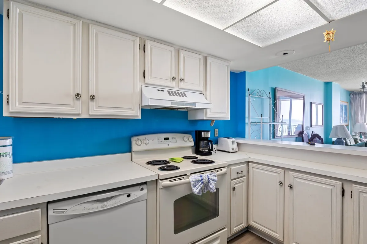 A cheerful kitchen interior featuring a blue accent wall, modern kitchen appliances, and crisp white cabinetry. The bright setting is designed for cooking and socializing, with visible counter space and a layout that encourages interaction.