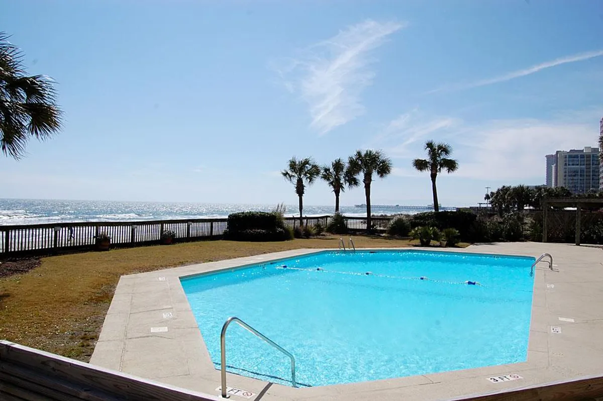 A beautiful exterior view of a sparkling swimming pool bordered by palm trees, with the vast ocean as a picturesque backdrop. The ambiance is tranquil and inviting, perfect for poolside relaxation with ocean breezes.