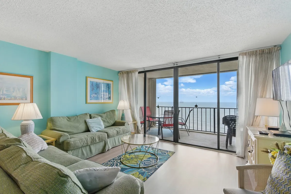 This image features a comfortable living area with a sofa positioned to take in the ocean view through wide windows. A coffee table sits in the center, and cheerful artwork decorates the wall, all set in a bright, inviting space ideal for relaxing or socializing.