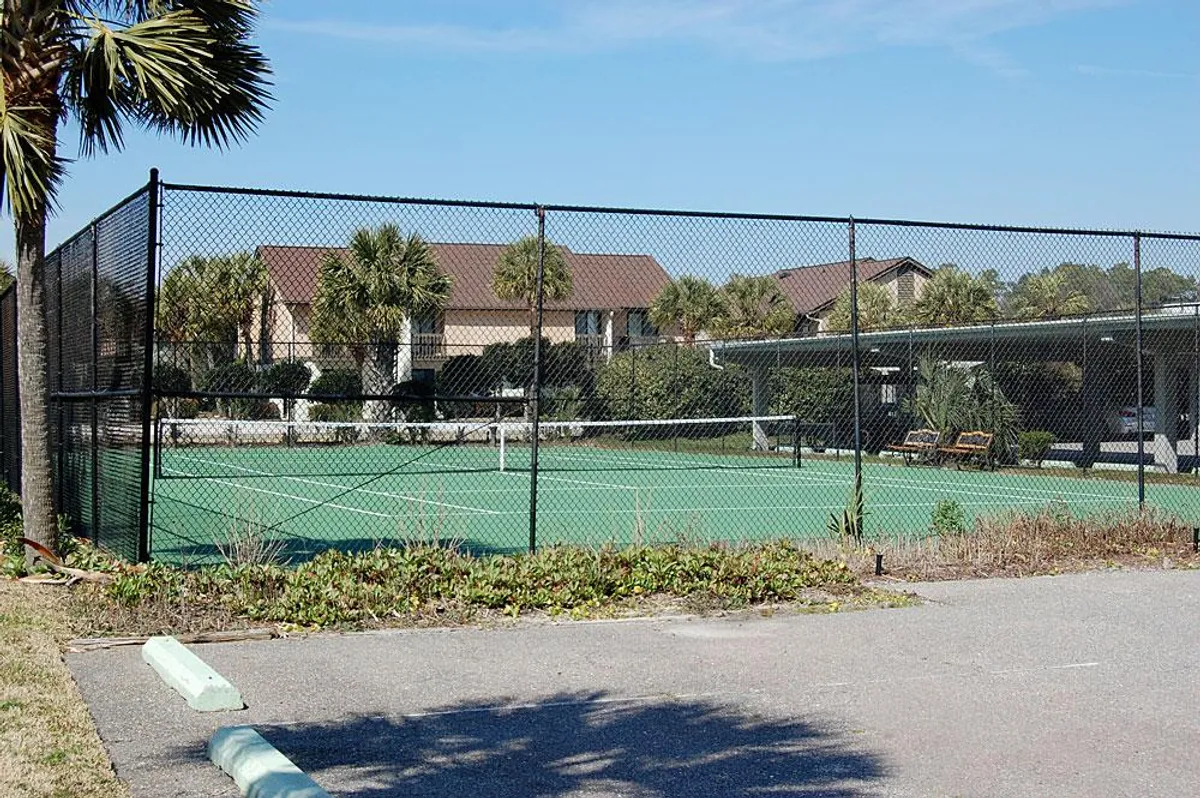 A well-maintained tennis court set among palm trees and surrounded by resort buildings. Benches offer spots for spectators or relaxing between matches, and the vibe is active yet leisurely.