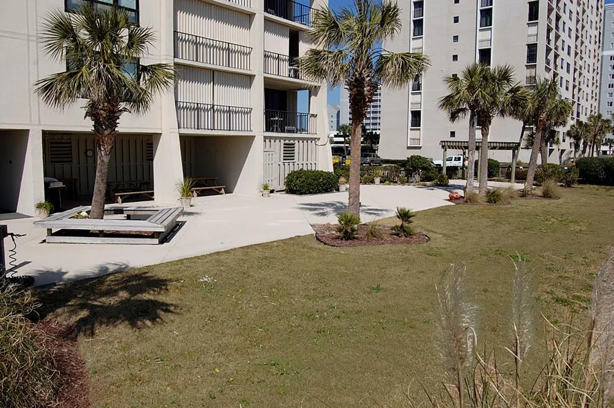 An inviting outdoor seating area surrounded by palm trees and the balconies of the condo building, suggesting opportunities for socializing or peaceful relaxation. The setting is bright and tranquil, ideal for enjoying the coastal breeze and outdoor meals.