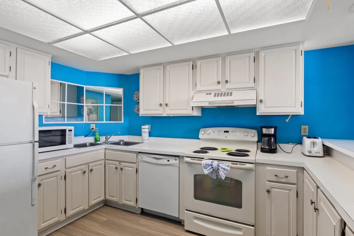 A vibrant kitchen space with bright blue walls, white cabinetry, stainless steel appliances, and a spacious countertop. The room is lively and welcoming, ideal for family gatherings and meal preparation.