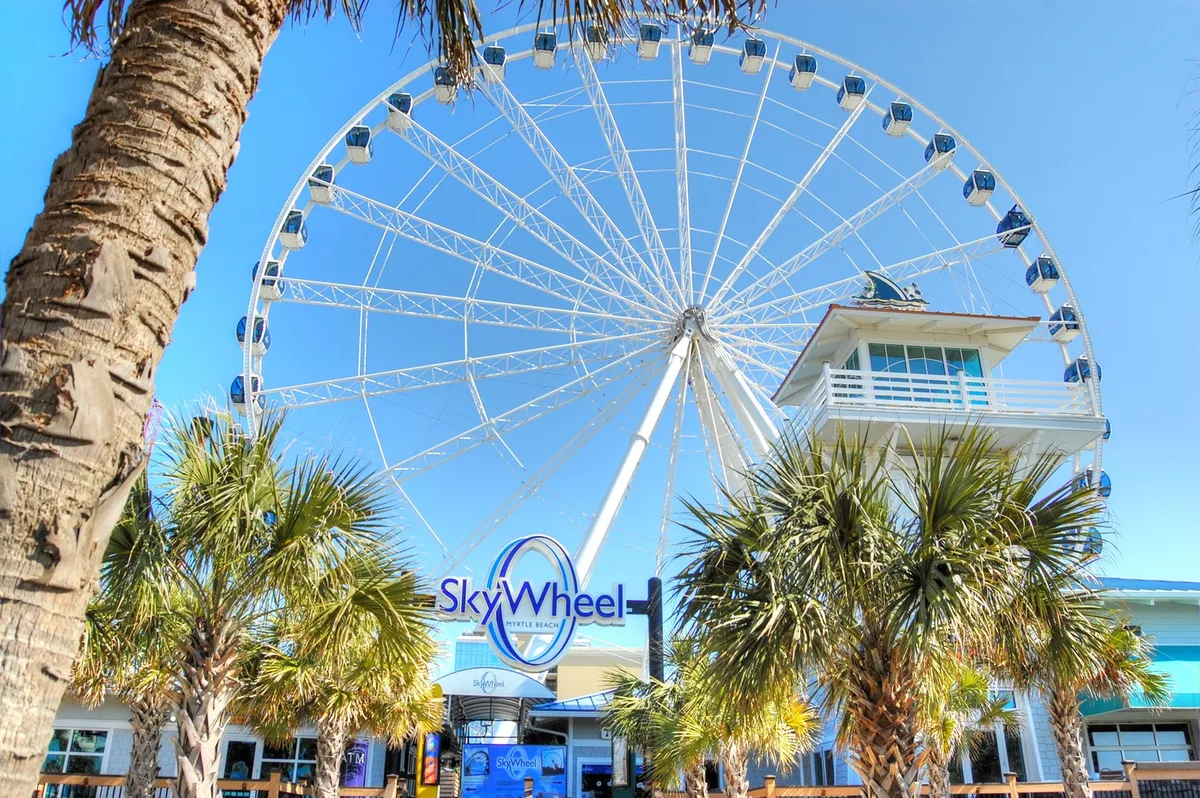A lively exterior shot of the iconic SkyWheel framed by palm trees and colorful signage, evoking the excitement of Myrtle Beach’s attractions. The image suggests opportunities for evening entertainment and memorable experiences just a short trip from the condo.